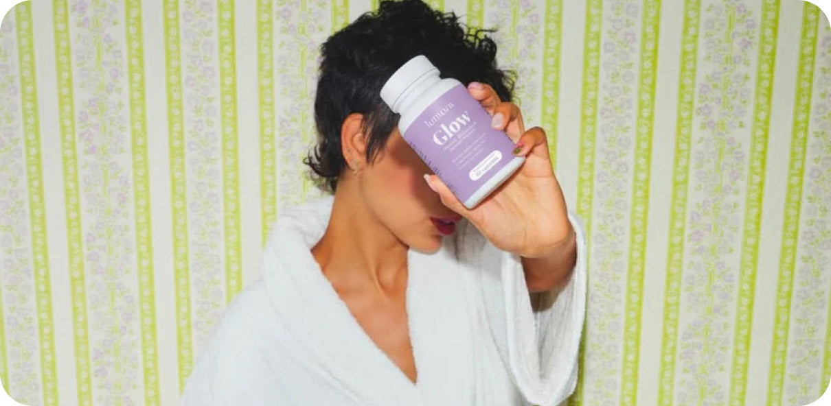 Woman in a bathrobe drinking from a Lumora Glow bottle