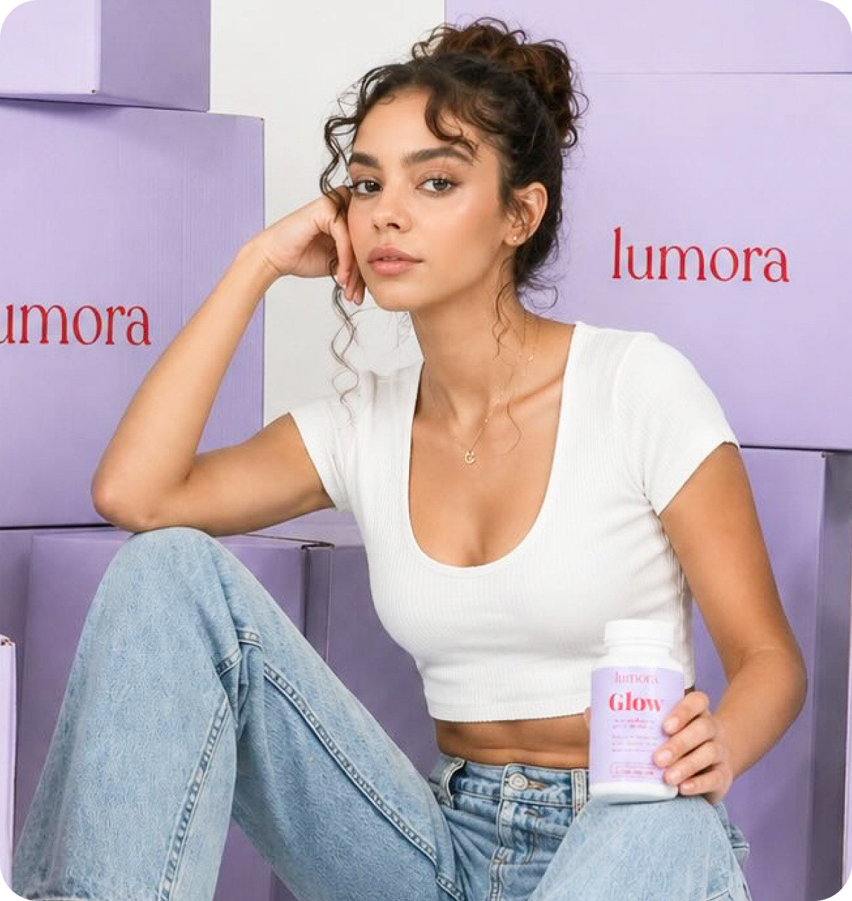 Woman sitting among Lumora product boxes, holding a bottle of Lumora Glow