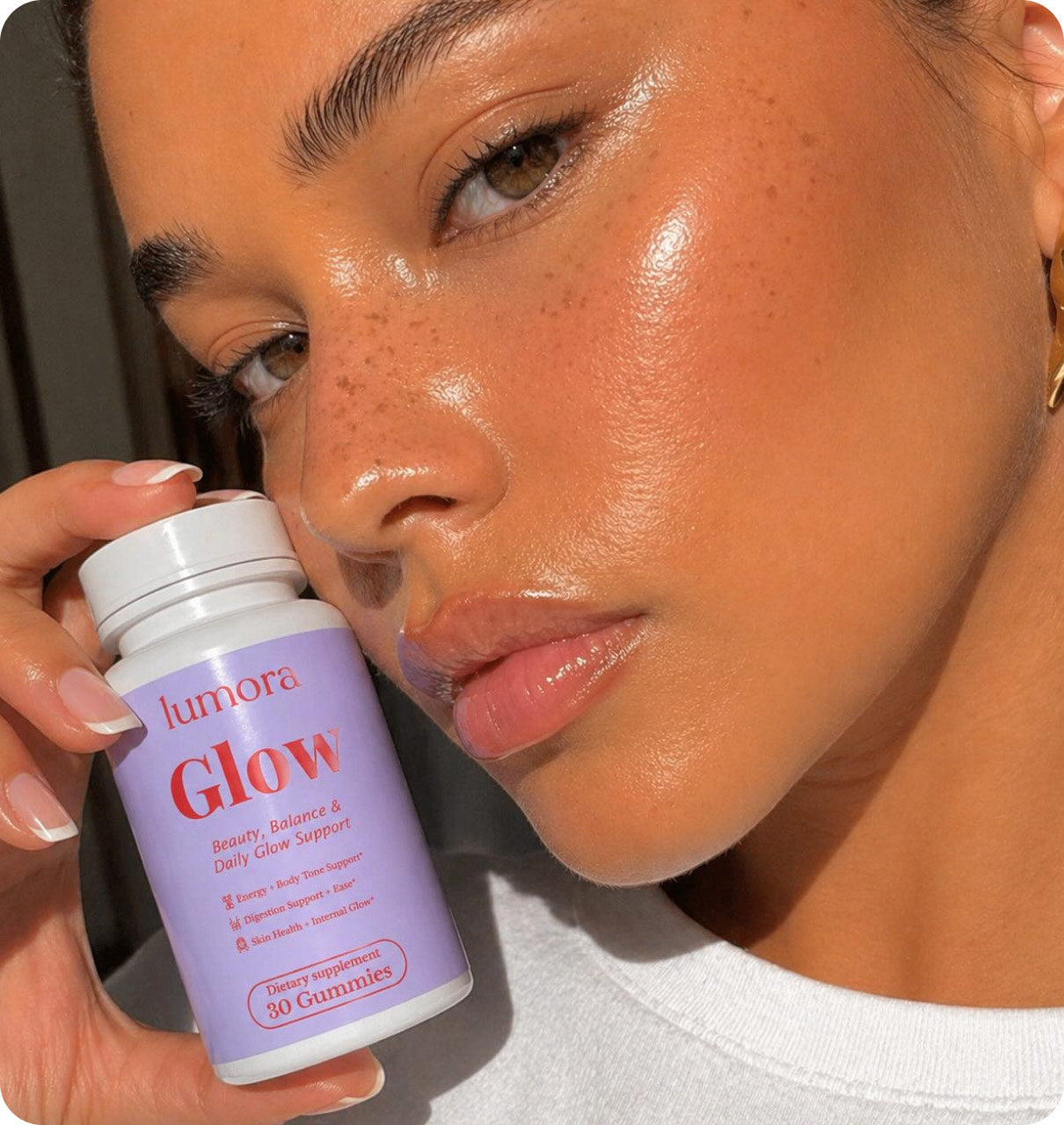 Close-up of a woman holding a bottle of Lumora Glow to her cheek
